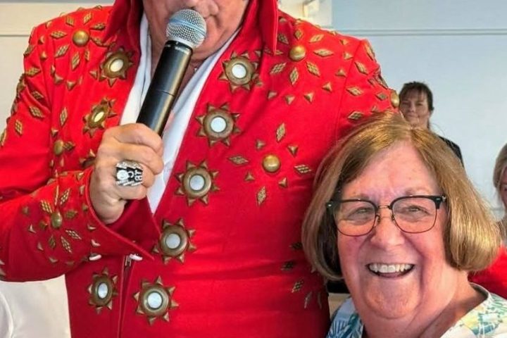 Woman smiling with man in red Elvis costume holding a microphone indoors.